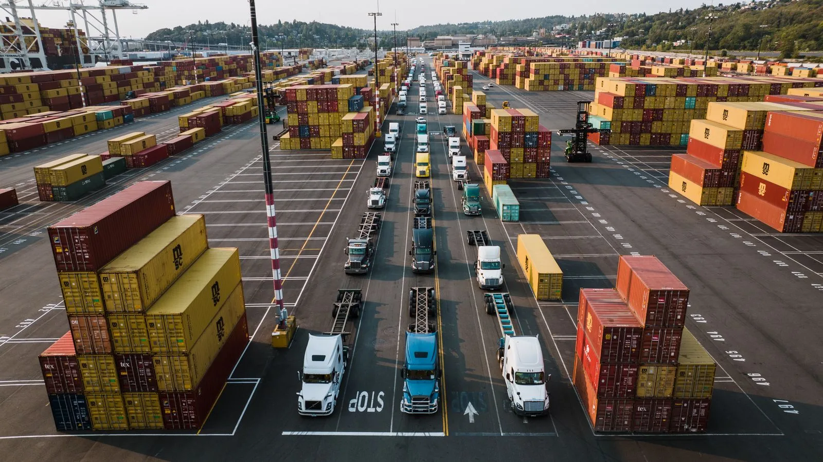 Aerial view of trucks lined up among colourful stacked cargo containers at a port